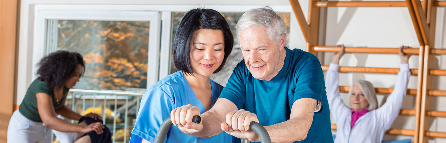 Elderly man exercising with nurse, others participating in therapy.